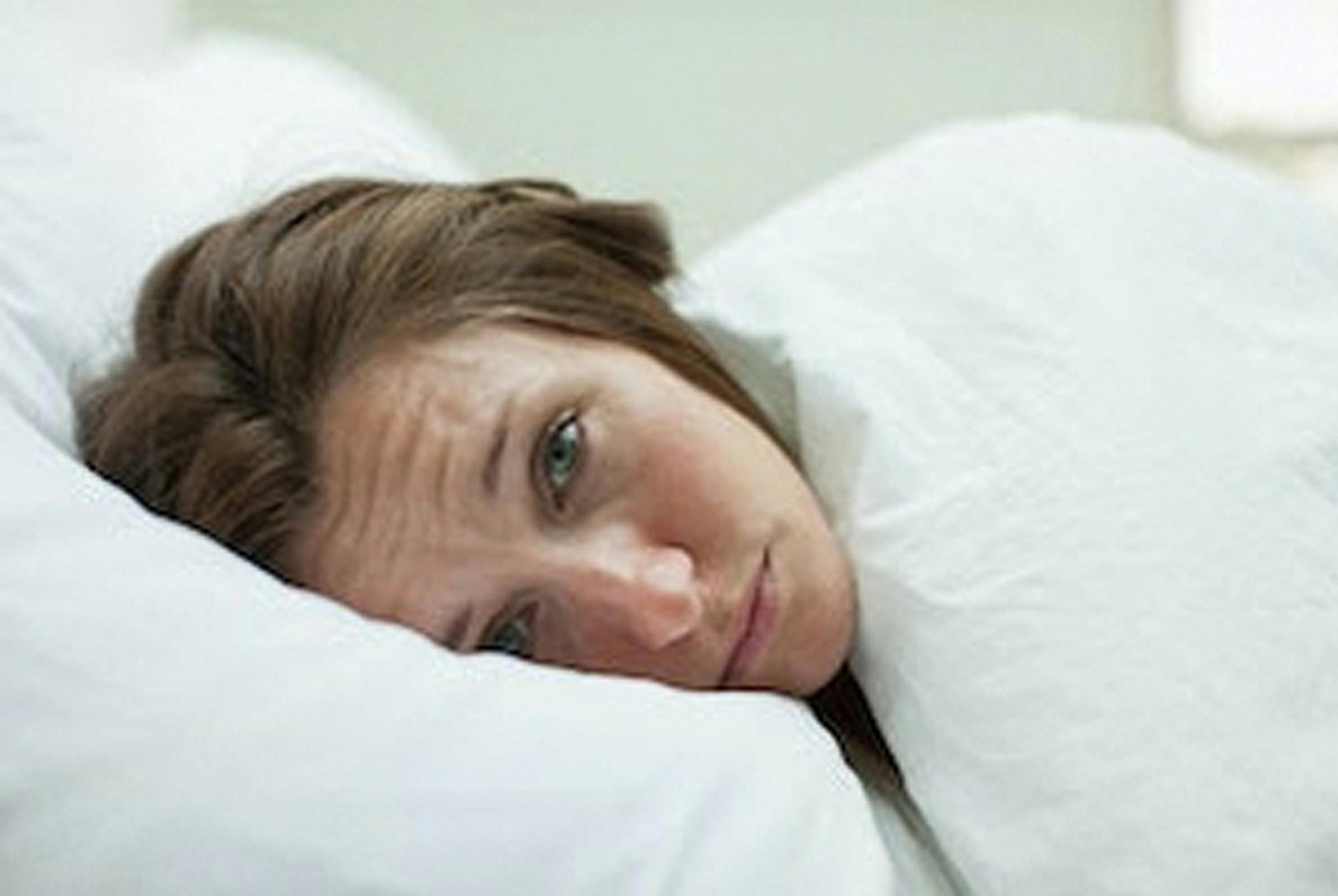 Stresset kvinde ligger søvnløs i sin seng.